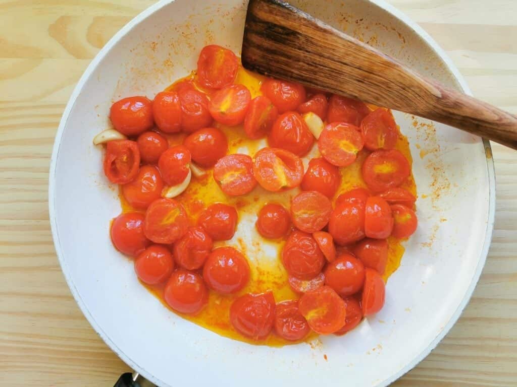 halved cherry tomatoes cooking in pan.