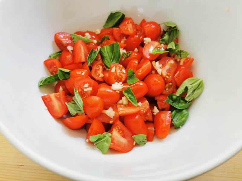 cut tomatoes in white bowl with basil, olive oil and garlic