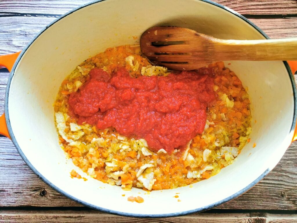 Tomato passata added to vegetables cooking in Dutch oven