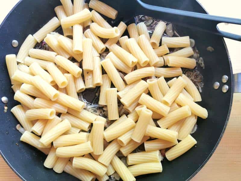 cooked elicoidali pasta added to skillet with onions and lardo