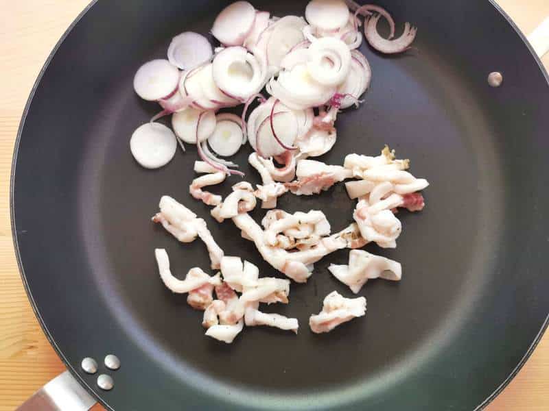 sliced Tropea onions and pieces of lardo in skillet