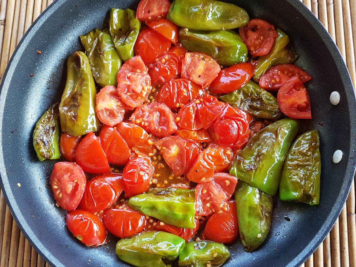 Cooked friggitelli peppers and tomatoes in a pan.