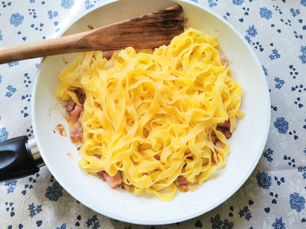 Cooked and drained fettuccine in pan with pancetta and onion.
