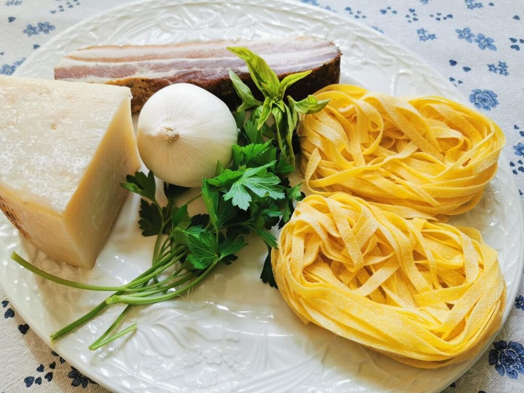 Ingredients for pasta with pancetta (fettuccine all’Abruzzese) on white plate.