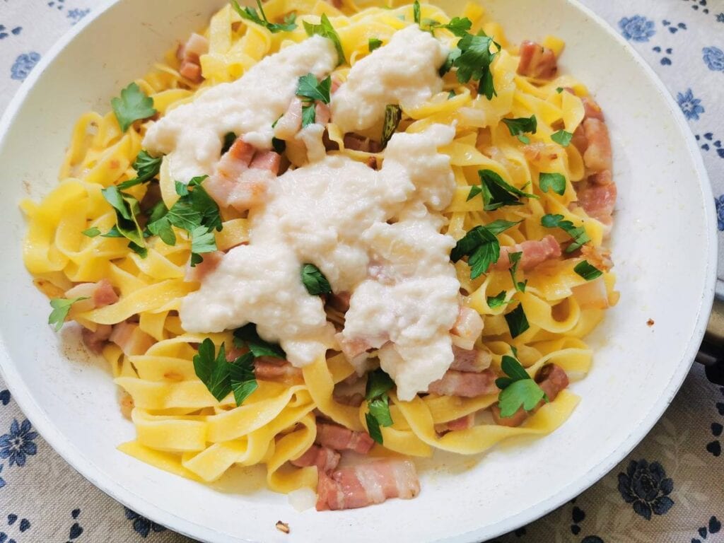 Pecorino cheese sauce added to pasta with pancetta in pan.