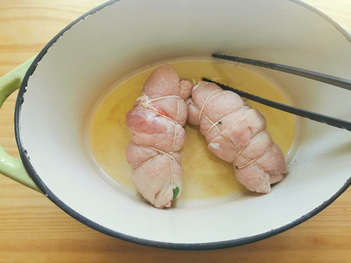 Two uncooked pork involtini (braciole) in Dutch oven with olive oil.