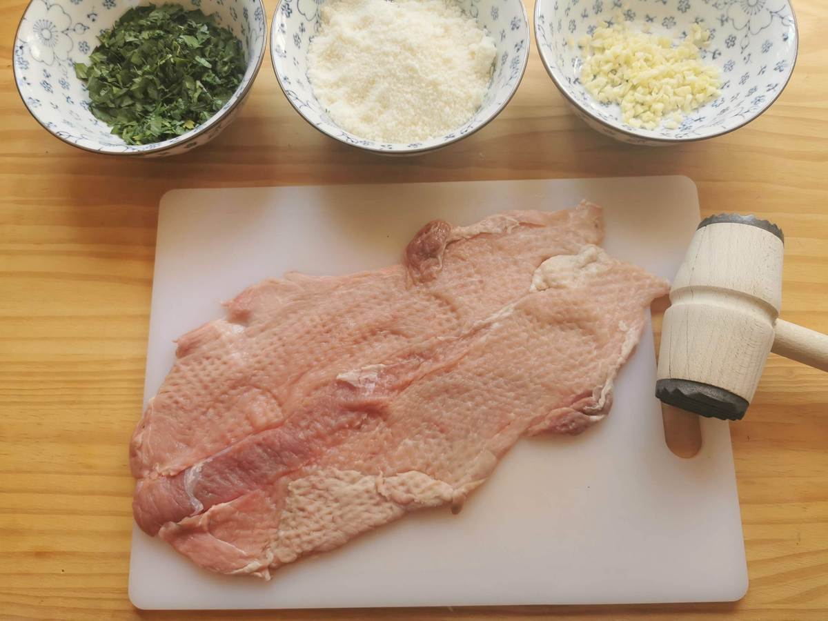 I slice of pork shouldeer that has been pounded with a meat hammer on white chopping board.