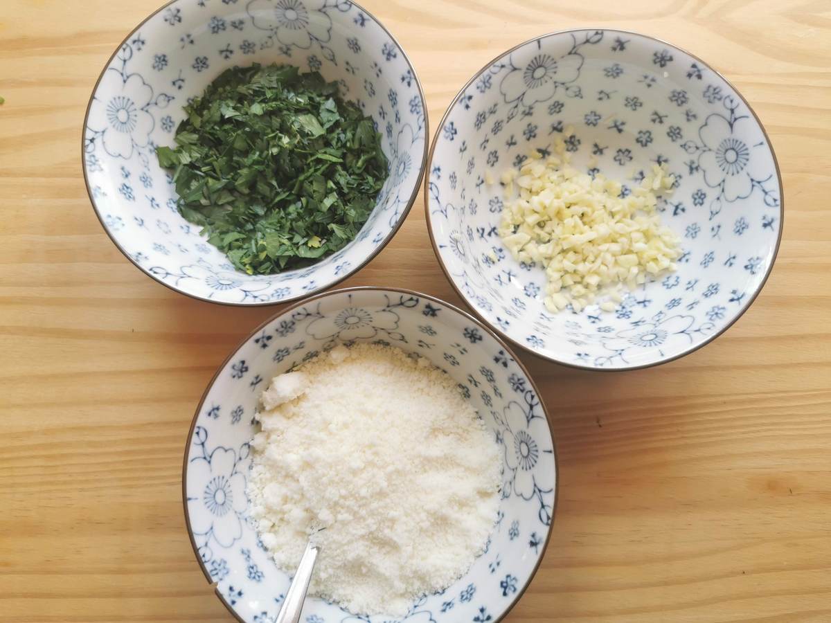 Chopped garlic, chopped fresh parsley and grated pecorino in separate blue and white bowls.
