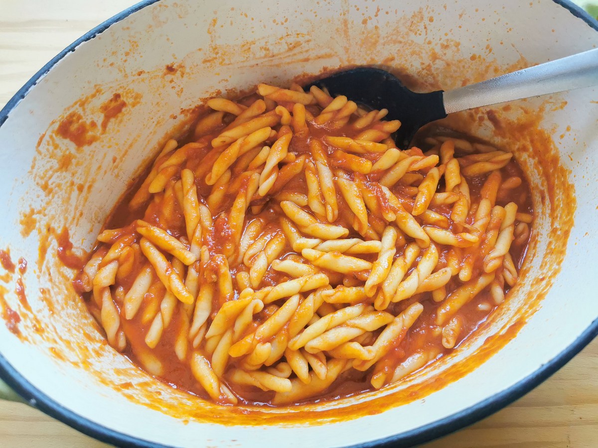 Cooked strozzapreti pasta mixed with tomato sauce in Dutch oven.