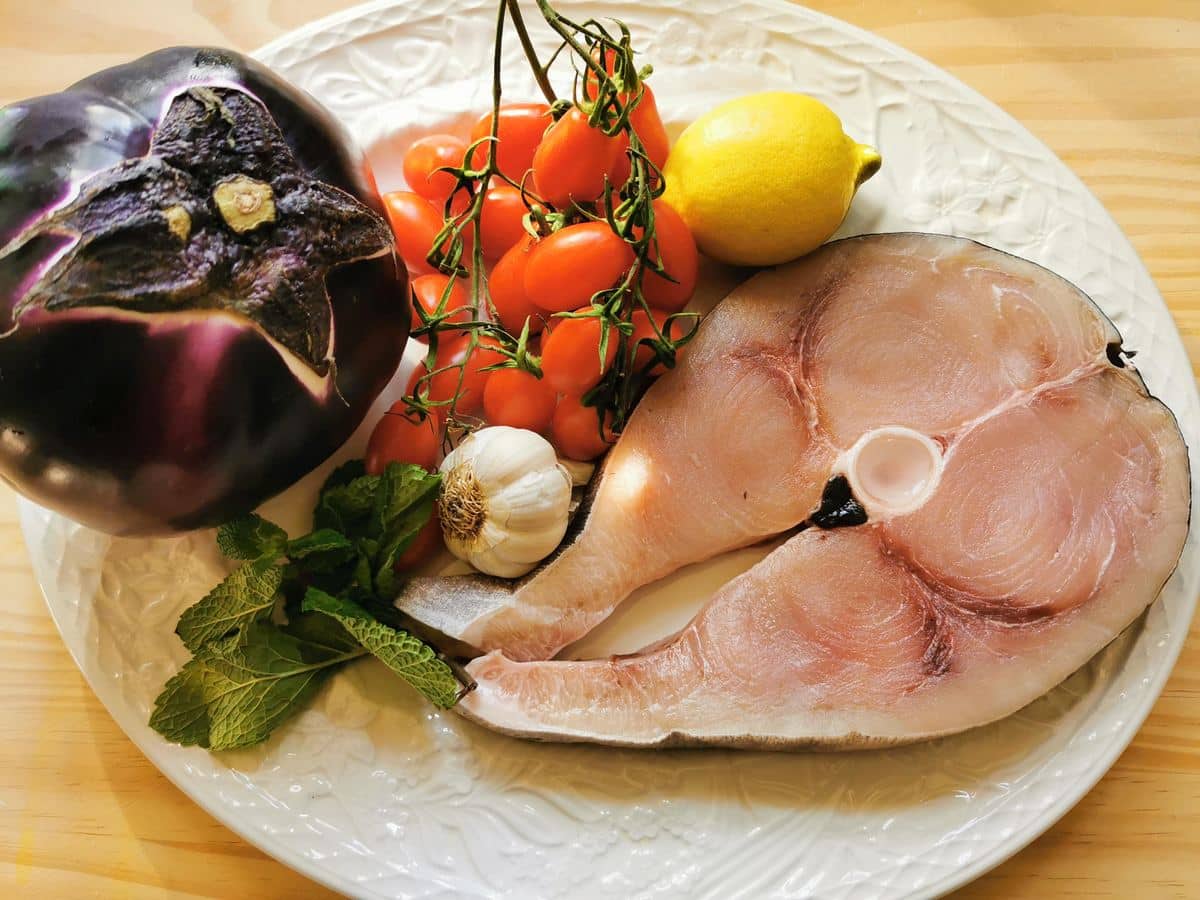 Swordfish, eggplant, cherry tomatoes, garlic, lemon and mint on a kitchen counter.