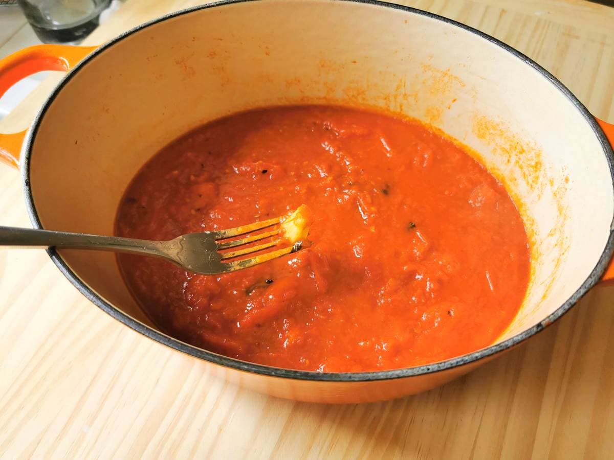 ready tomato sauce in Dutch oven with garlic clove on the end of a fork