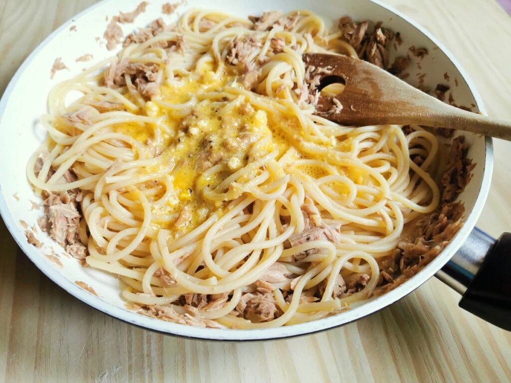 beaten eggs and cheese added to pasta and tuna in pan.