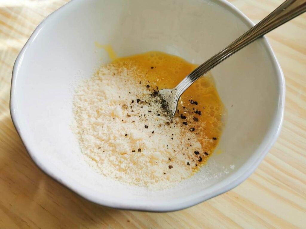 beaten eggs with grated parmigiano in white bowl