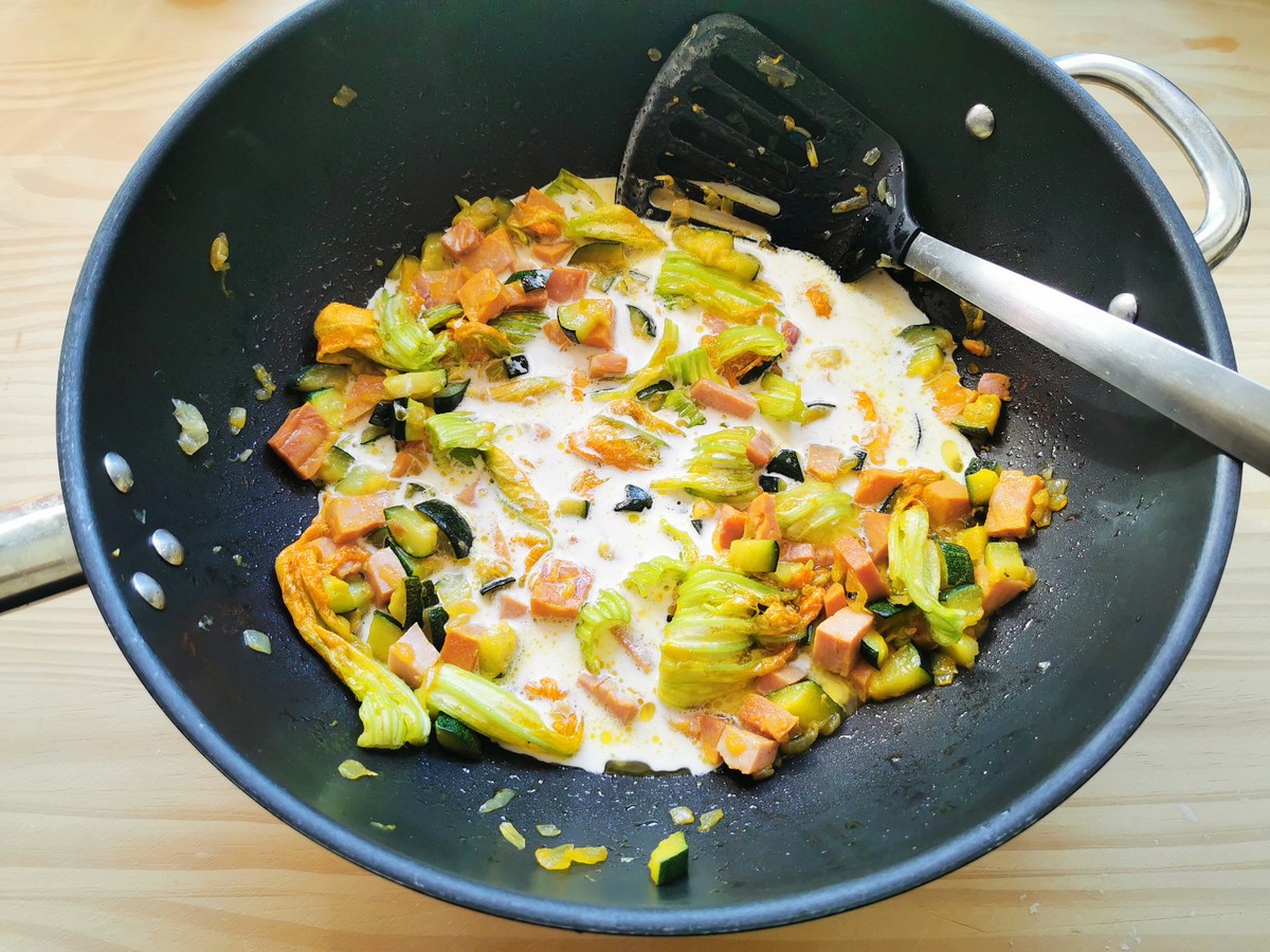 Cream added to zucchini flower pasta sauce ingredients in skillet.