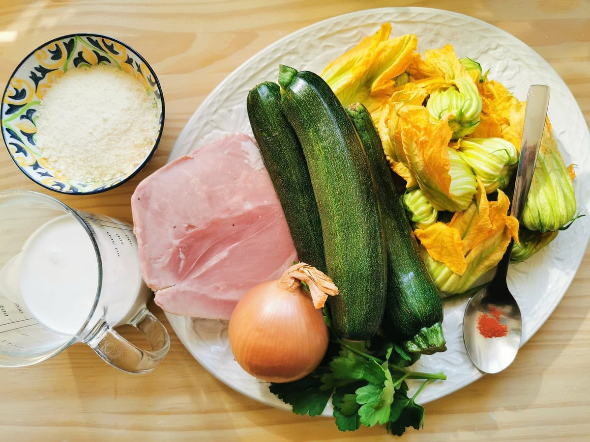 Ingredients for pasta with zucchini flowers on white plate.
