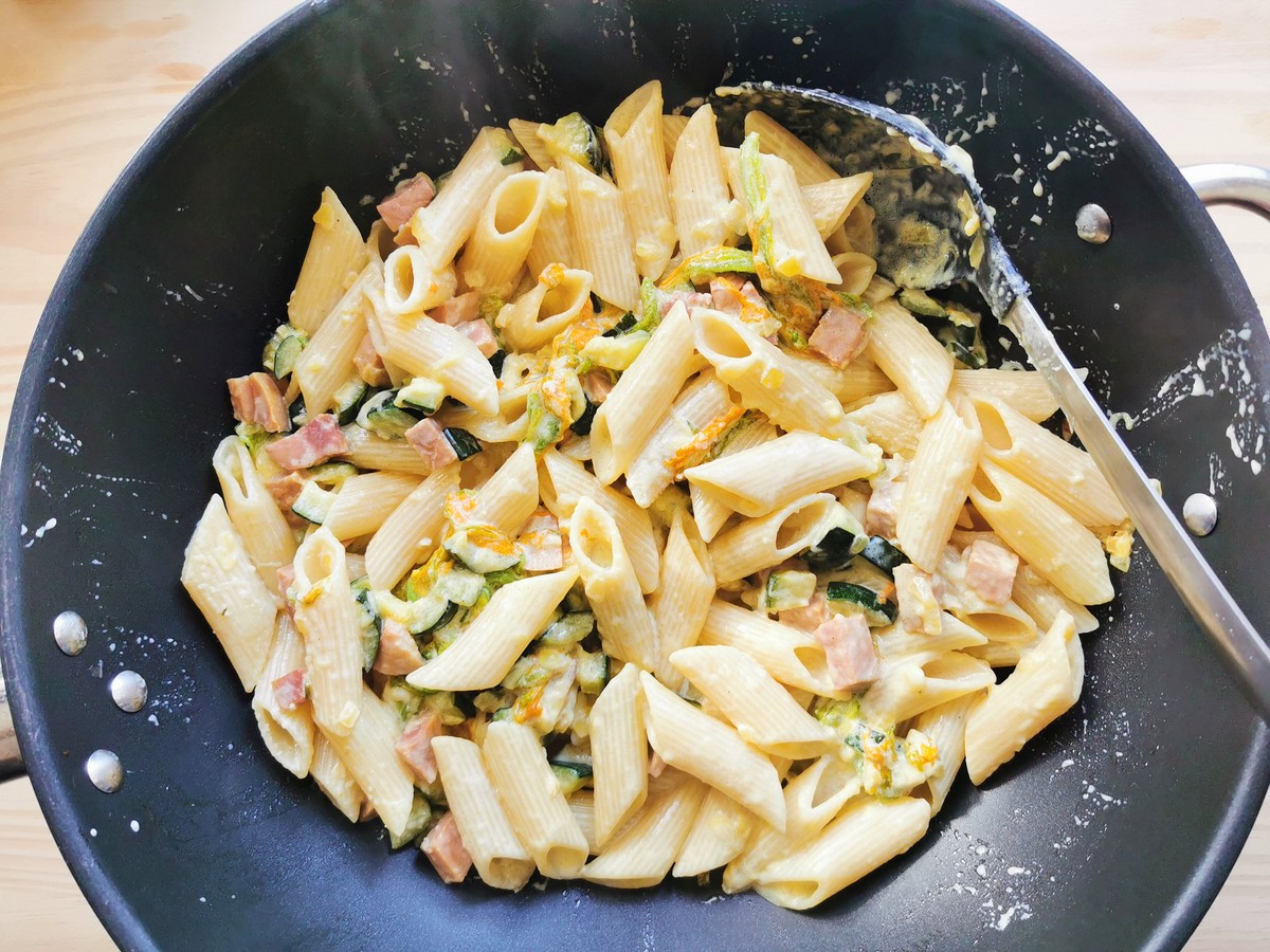 Ready pasta with zucchini flowers, saffron and ham in skillet.