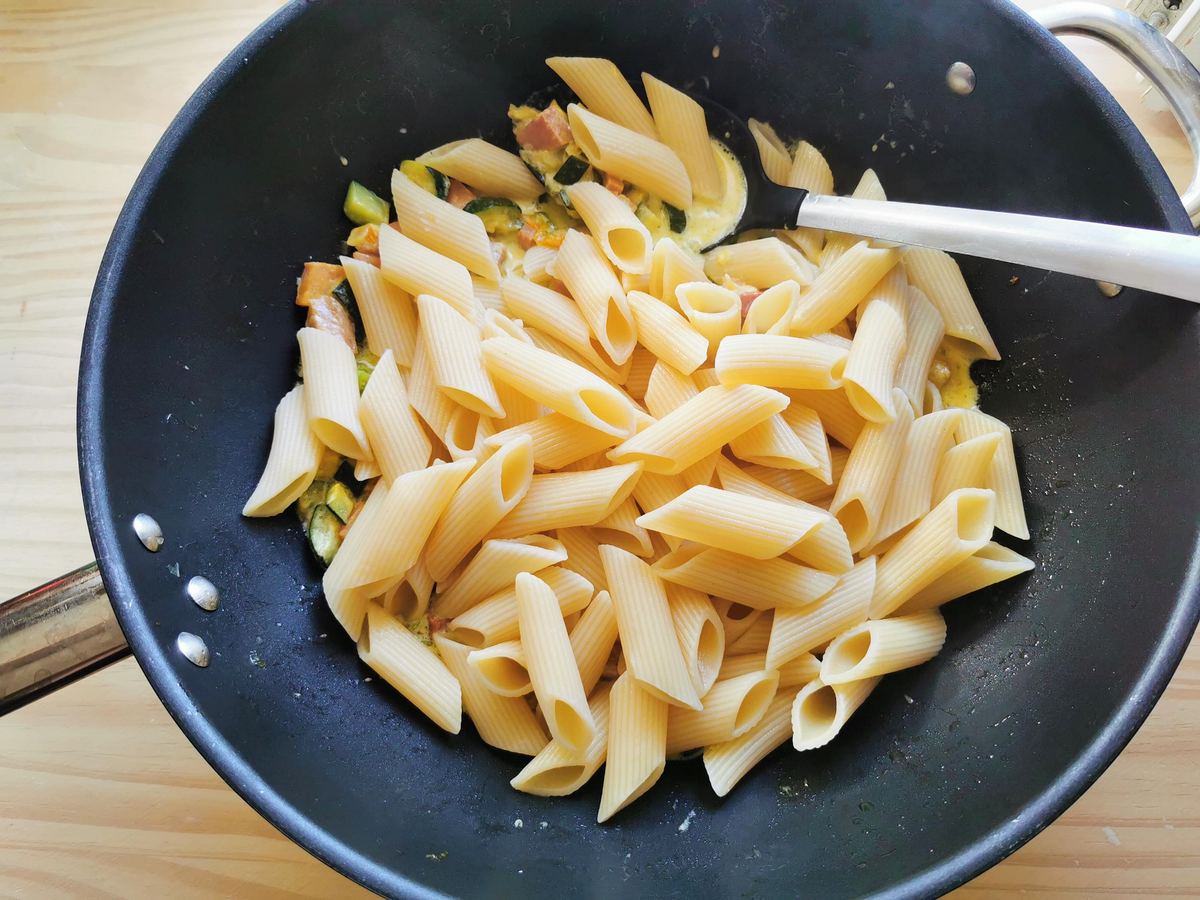 Cooked and drained pennoni pasta in skillet with zucchini flower pasta sauce.