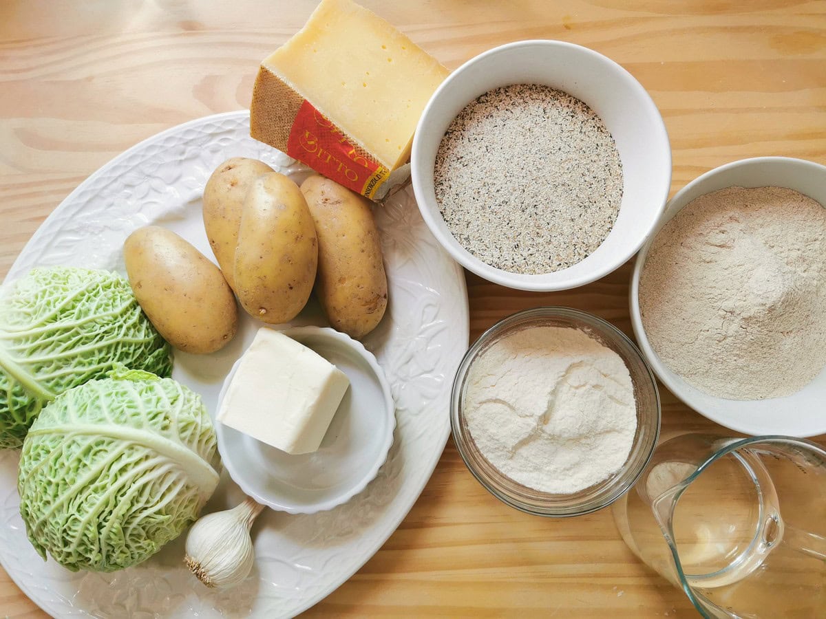Ingredients for homemade pizzoccheri alla Valtellinese pasta and the condiment on wood worktop.