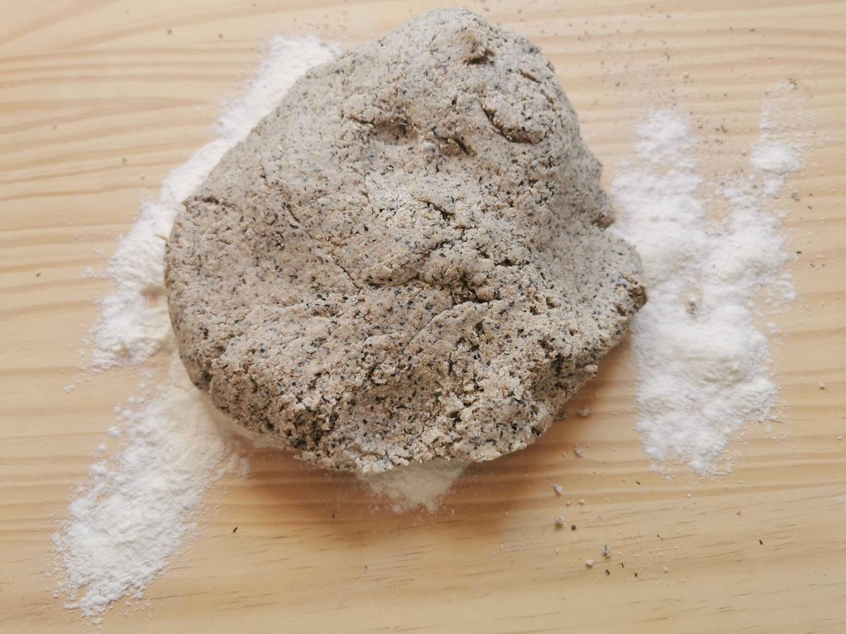 A ball of pizzoccheri pasta dough on a wood work top sprinkled with white flour.