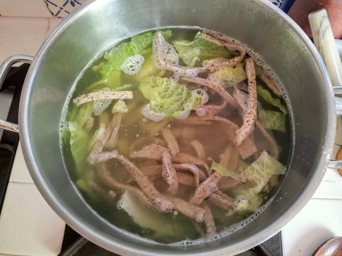 Homemade pizzoccheri pasta cooking in large pot of water with savoy cabbage and potatoes.