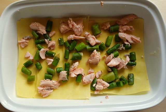 Poached salmon and asparagus lasagne al forno being assembled in white oven dish