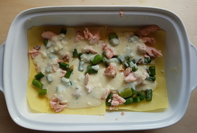Poached salmon and asparagus lasagne al forno being assembled in white oven dish