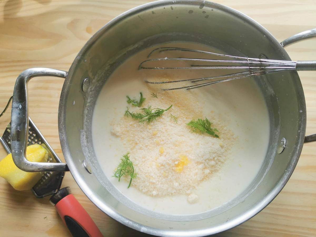Ready béchamel in saucepan with grated parmigiano, grated lemon zest and chopped dill on top.