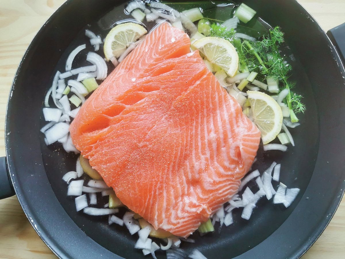 Fresh salmon fillet in poaching pan with onion, celery, lemon slices and  fennel fronds.