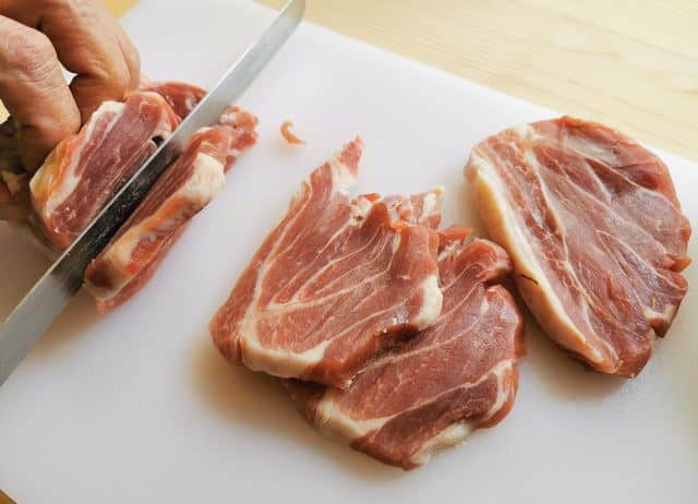 cutting prosciutto crudo ham end into thick slices