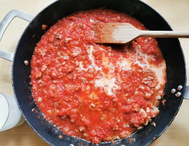 adding milk to the prosciutto ragu in skillet