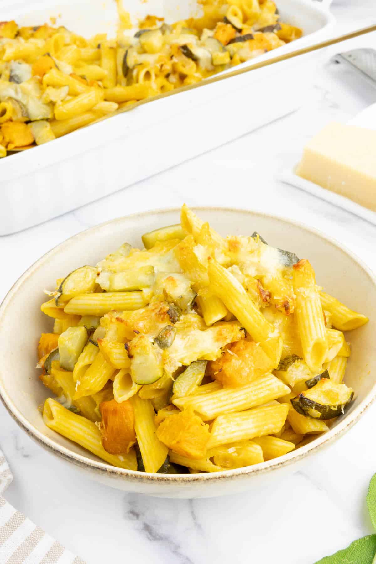 A serving of baked pumpkin pasta next to the baking dish