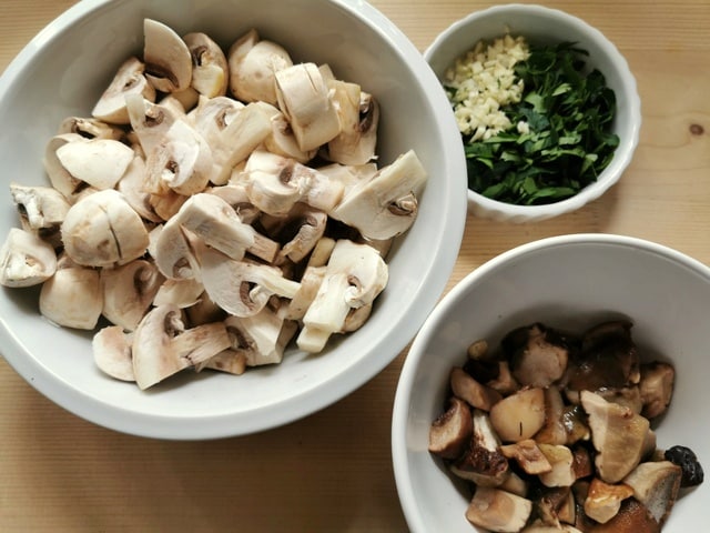 chopped frozen porcini, white champignon mushrooms, parsley and garlic in white bowls