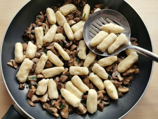 cooked ricotta gnocchi added to mushrooms in frying pan