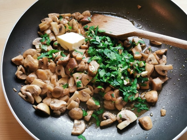 parsley and butter added to mushrooms cooking in frying pan