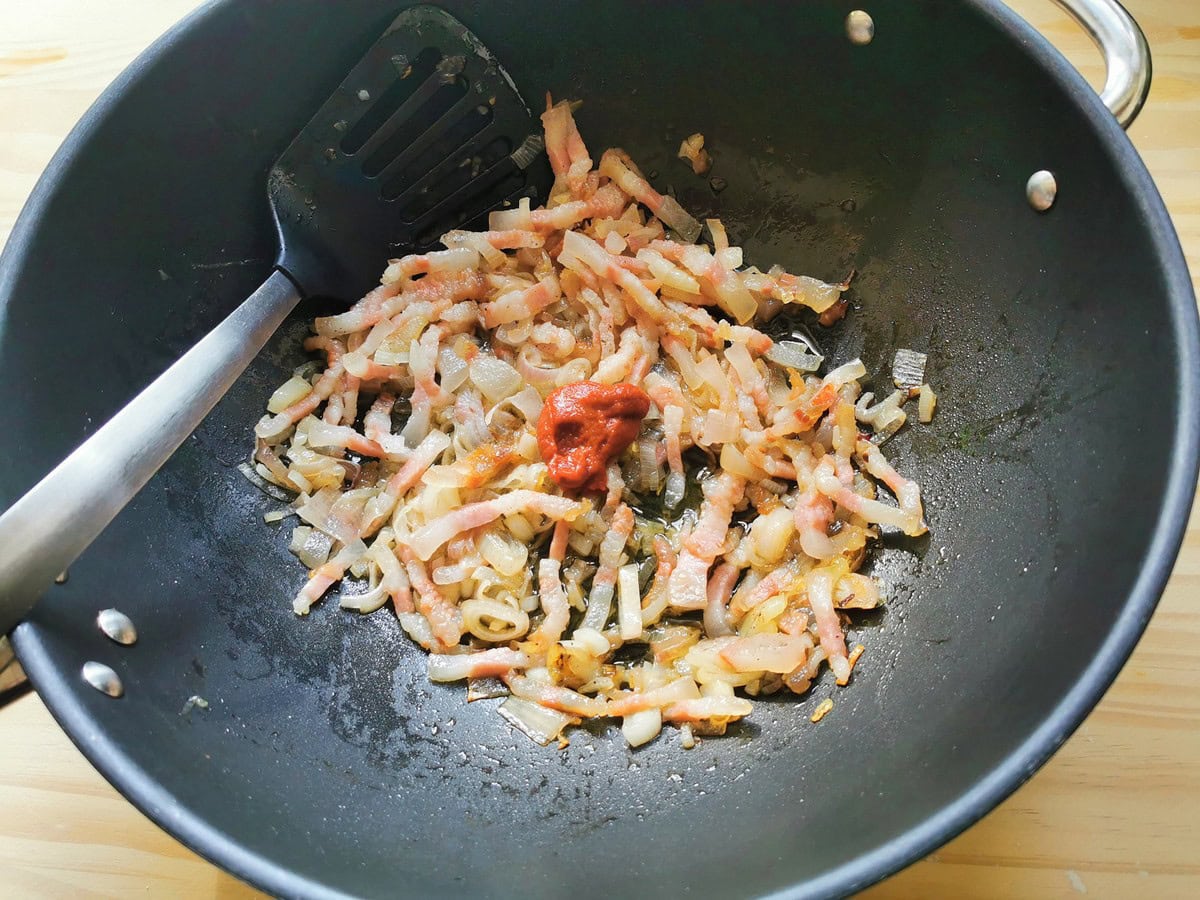 Tomato paste added to shallots and guanciale in deep frying pan.