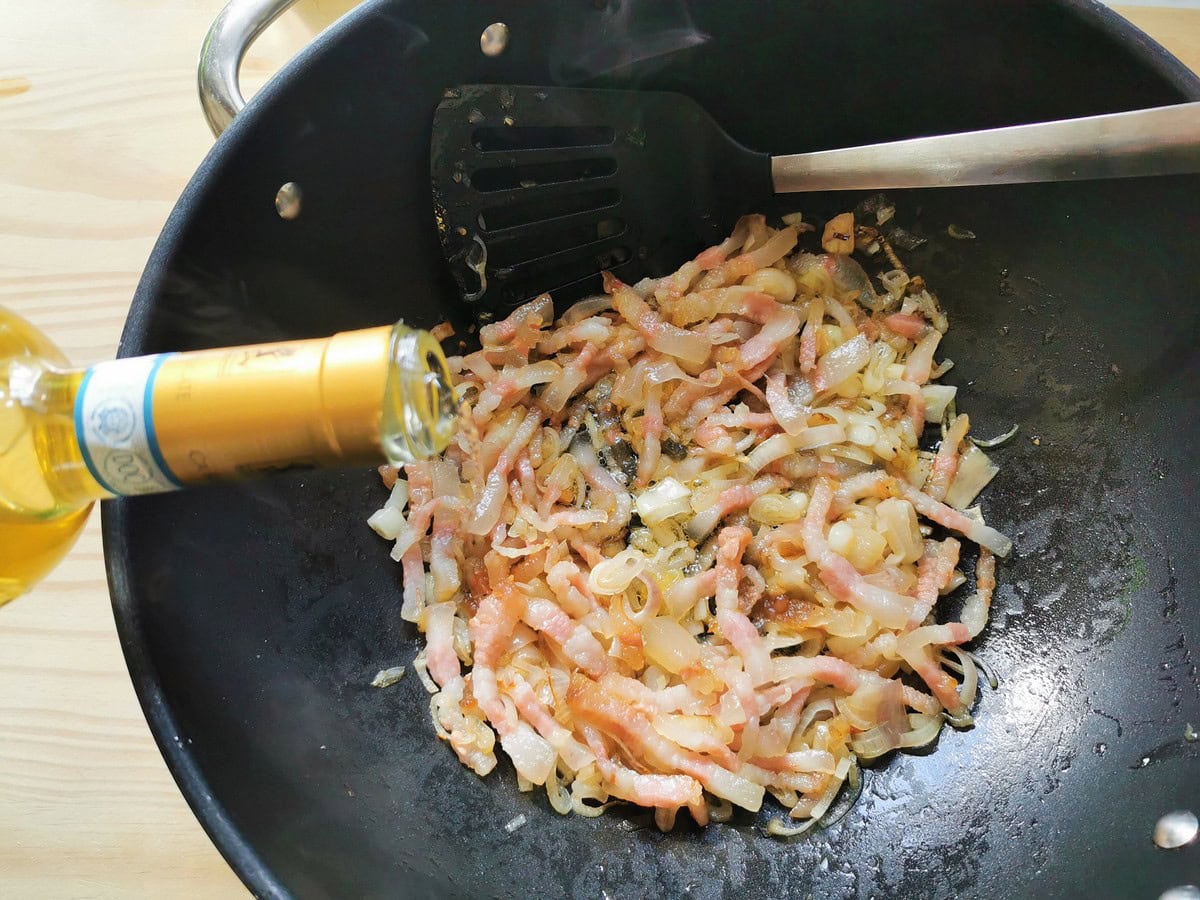 White wine being added to shallots and guanciale in deep frying pan.