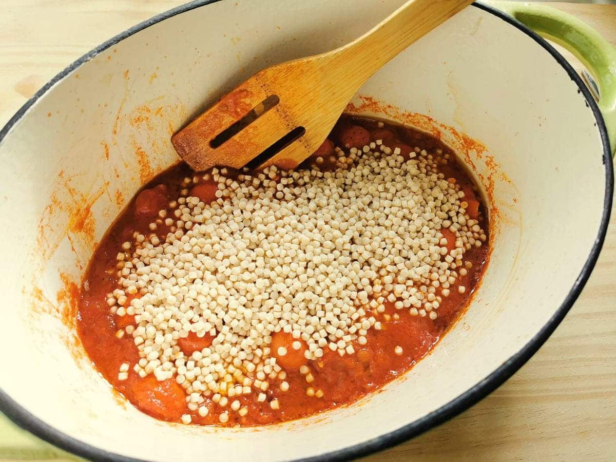 Dried fregola added to the tomato sauce in the Dutch oven.