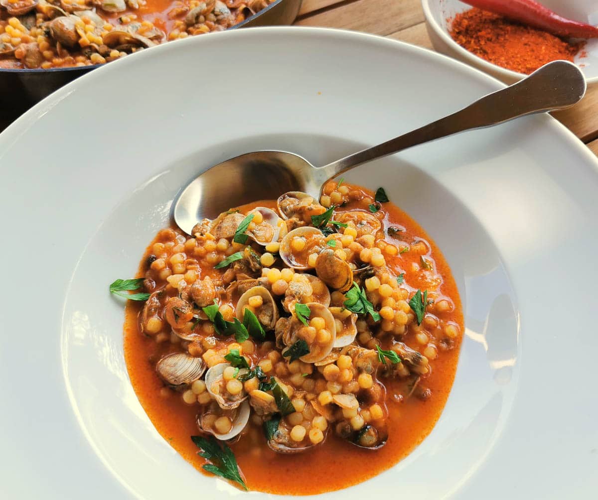 Fregola with clams in a bowl with parsley