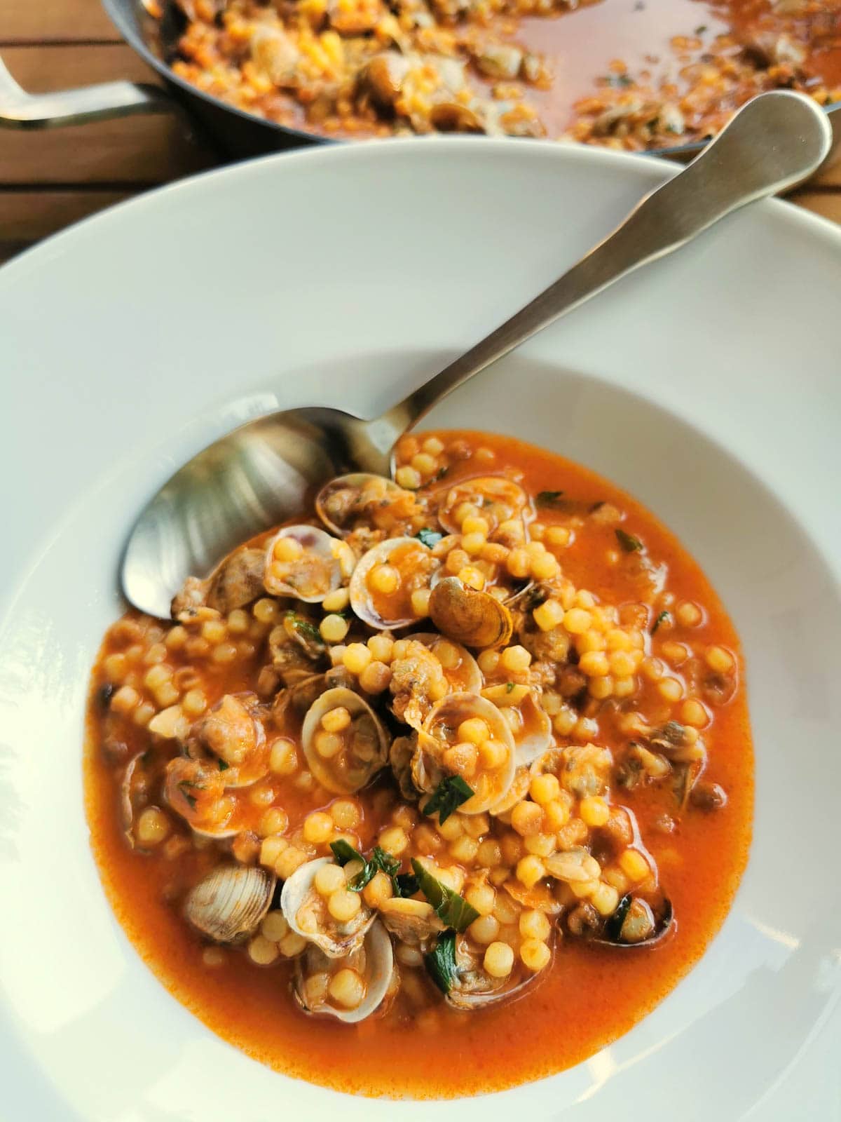 Fregola with clams in a bowl with a tablespoon