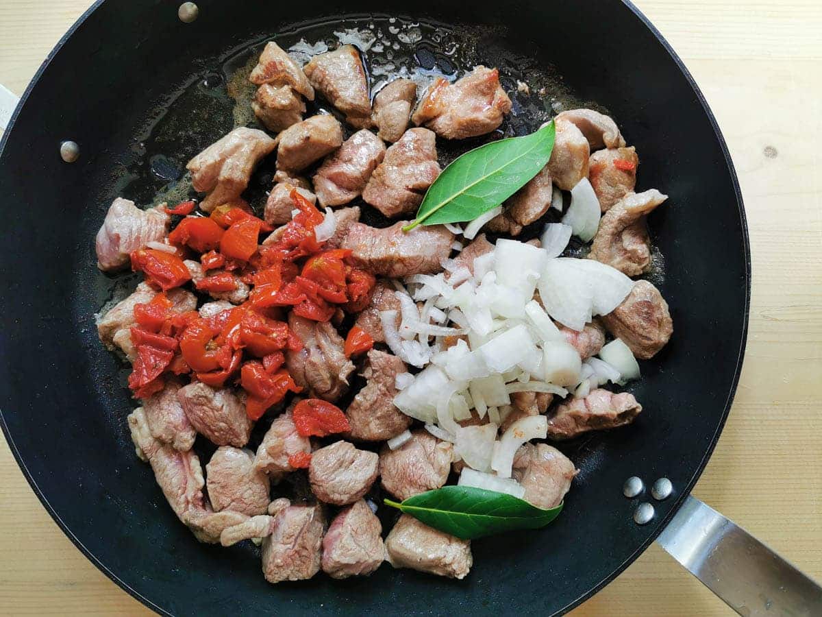 Chopped onions, bay leafs and chopped sun dried tomatoes in a skillet with lamb