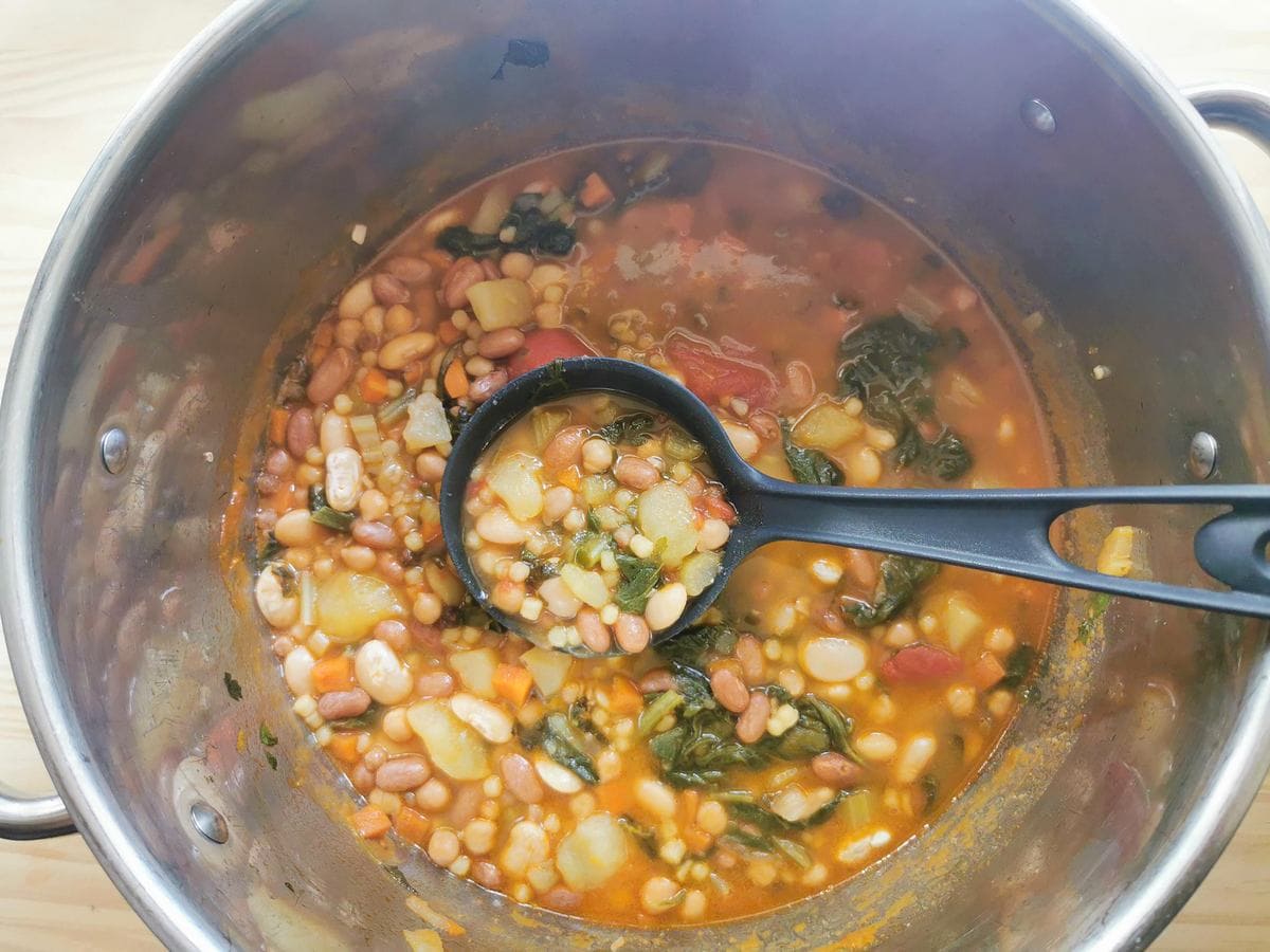 Ready cooked Sardinian longevity minestrone soup in large pot with ladle.