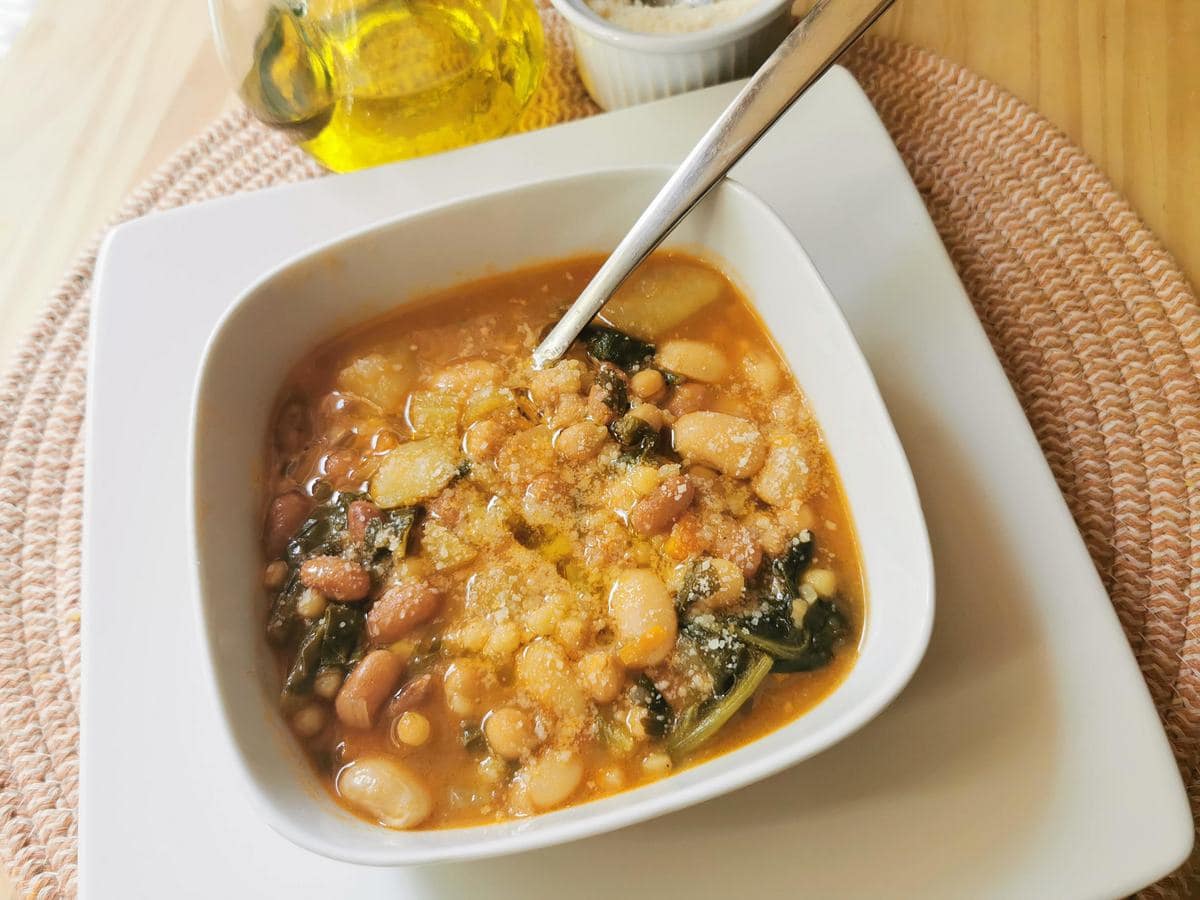 Sardinian minestrone soup with olive oil and grated pecorino on top in white bowl.