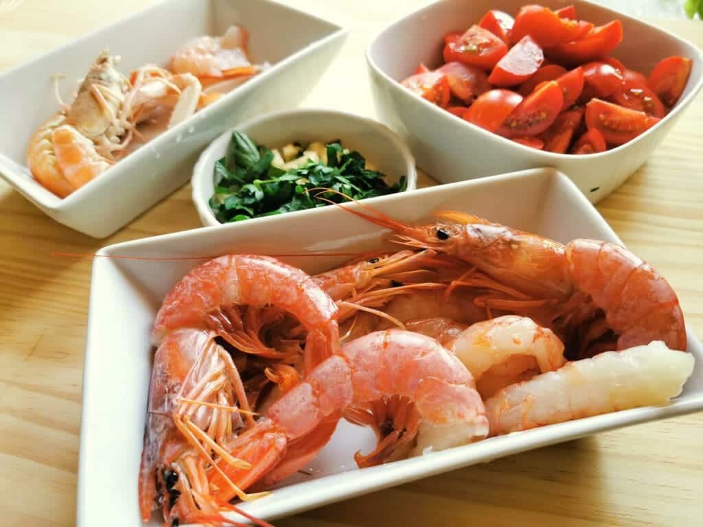 peeled and whole prawns in white bowl with chopped tomatoes in white bowl and peeled and whole scampi in white bowl