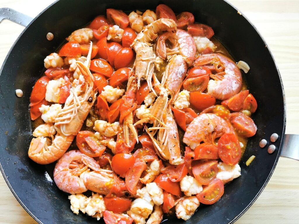 peeled shellfish pieces in skillet with whole shellfish and tomatoes