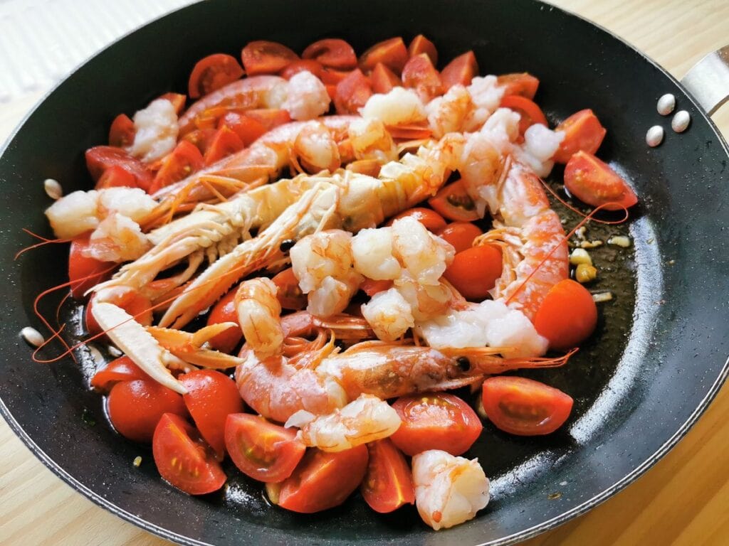 peeled shellfish pieces in skillet with whole shellfish and tomatoes