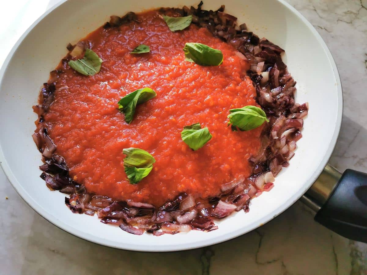 tomato passata in frying pan with onions and basil leaves