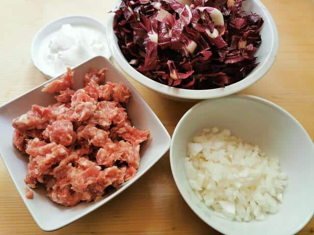 chopped sausage meat in white bowl. chopped radicchio in white bowl. peeled and chopped onion in white bowl