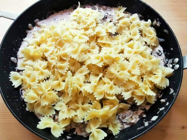 cooked farfalle pasta added to sausage and radicchio sauce in skillet
