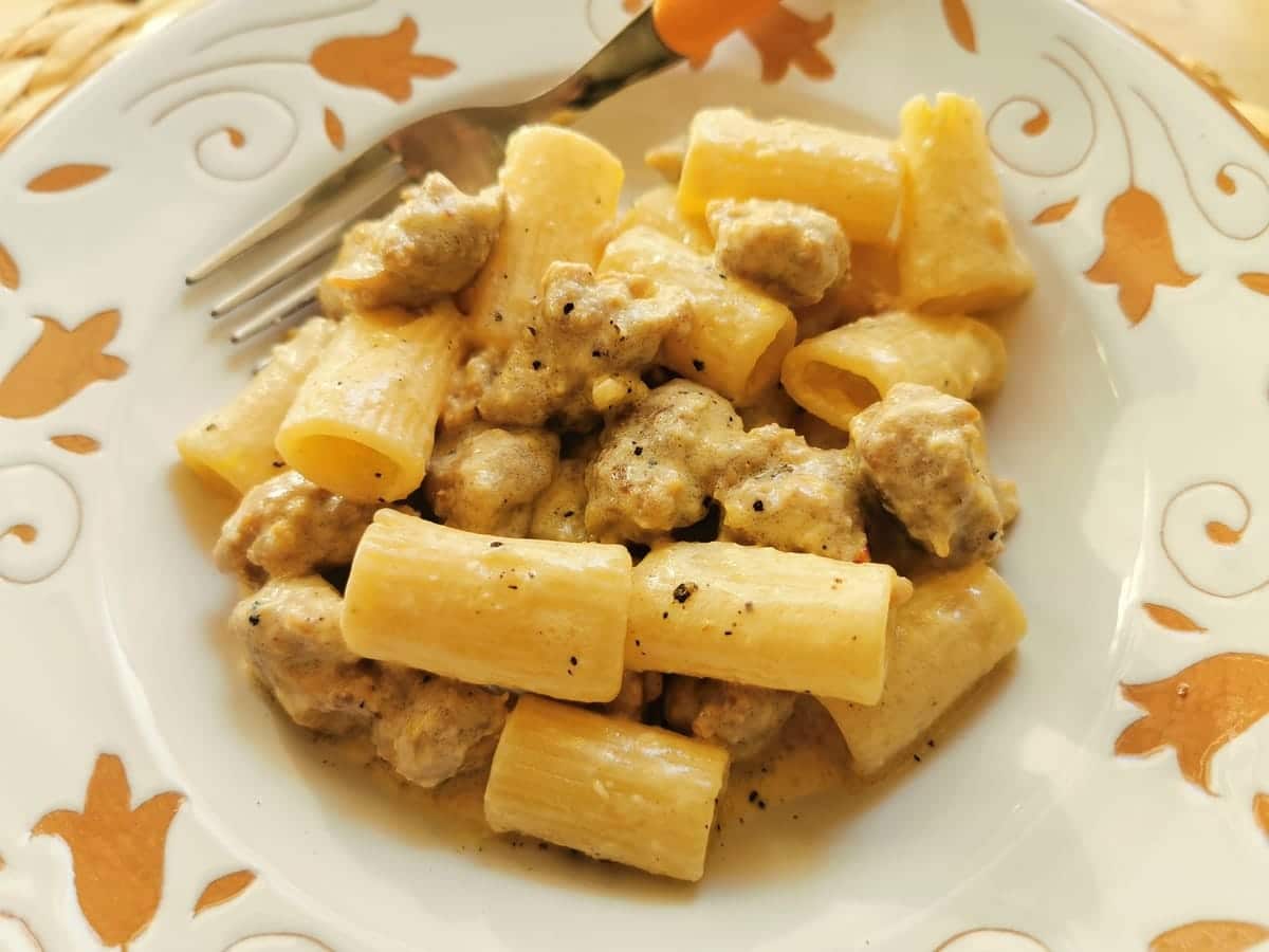 A serving of sausage and saffron pasta alla Monzese in a white bowl with a fork.