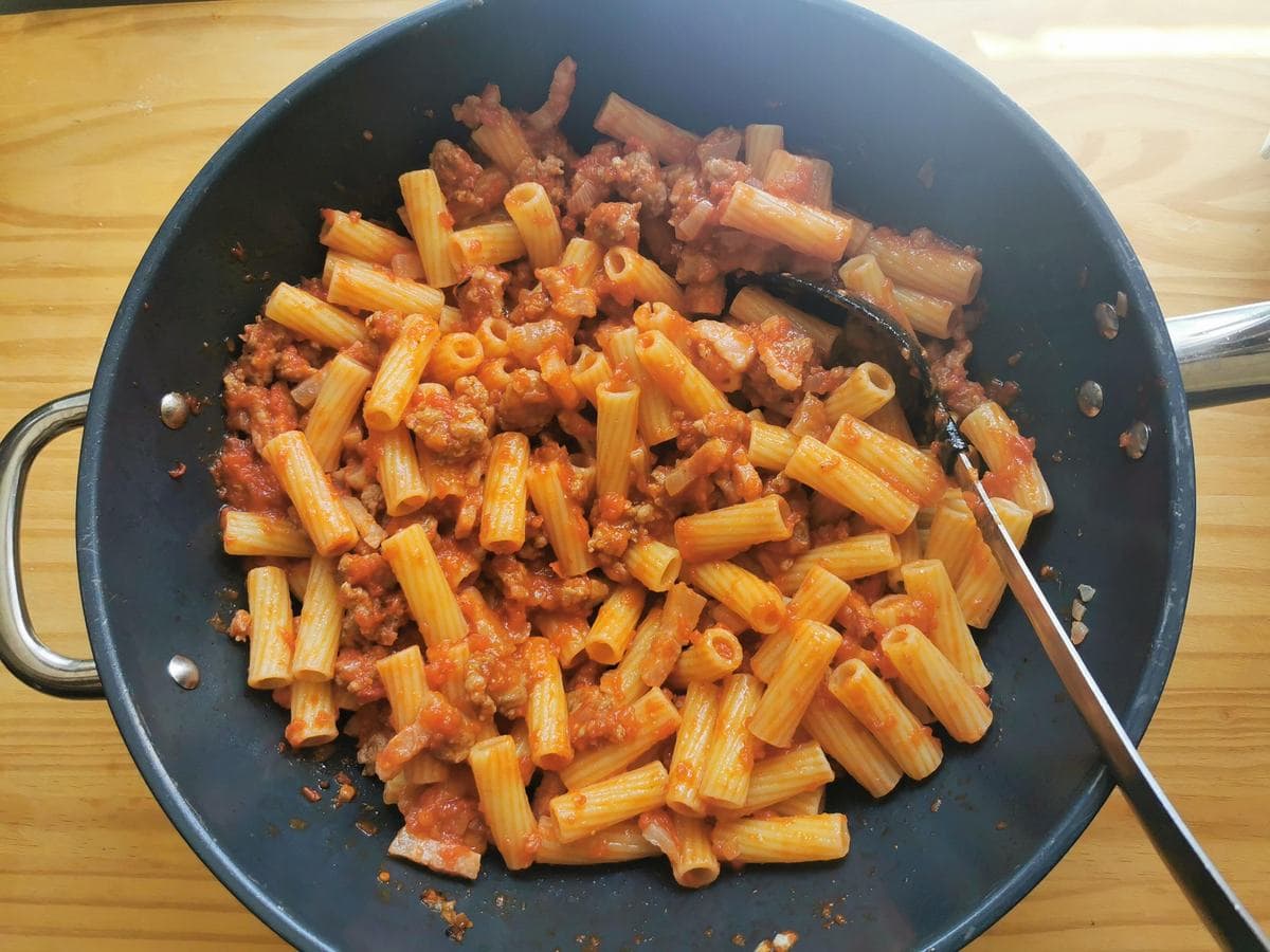 Cooked rigatoni mixed with sausage ragu in skillet.